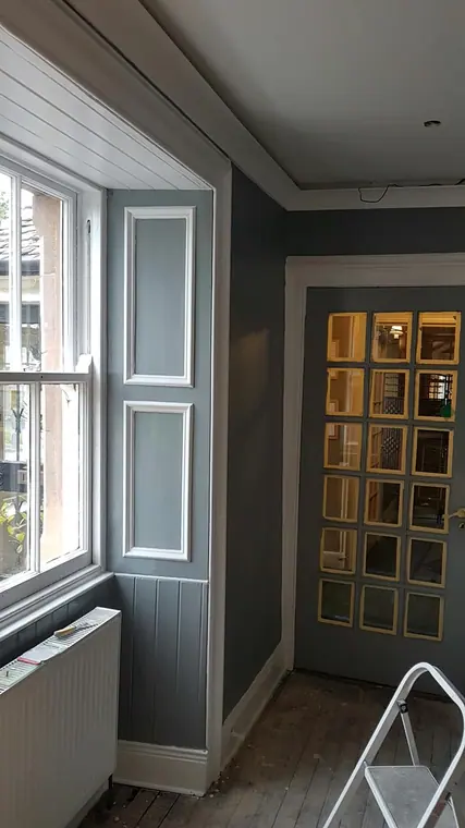A sash window with painted panelling below and a glazed door beyond, in grey and white.