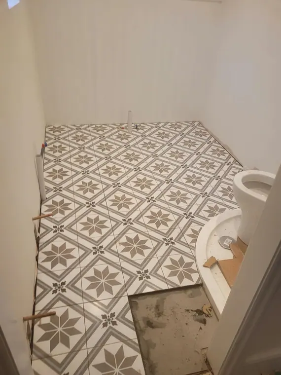 Patterned tiles going down in a small cloakroom, cut round the WC.