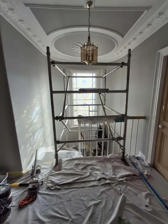 A scaffold tower under the ornate ceiling rose. High ceilings get a proper platform, not a ladder.